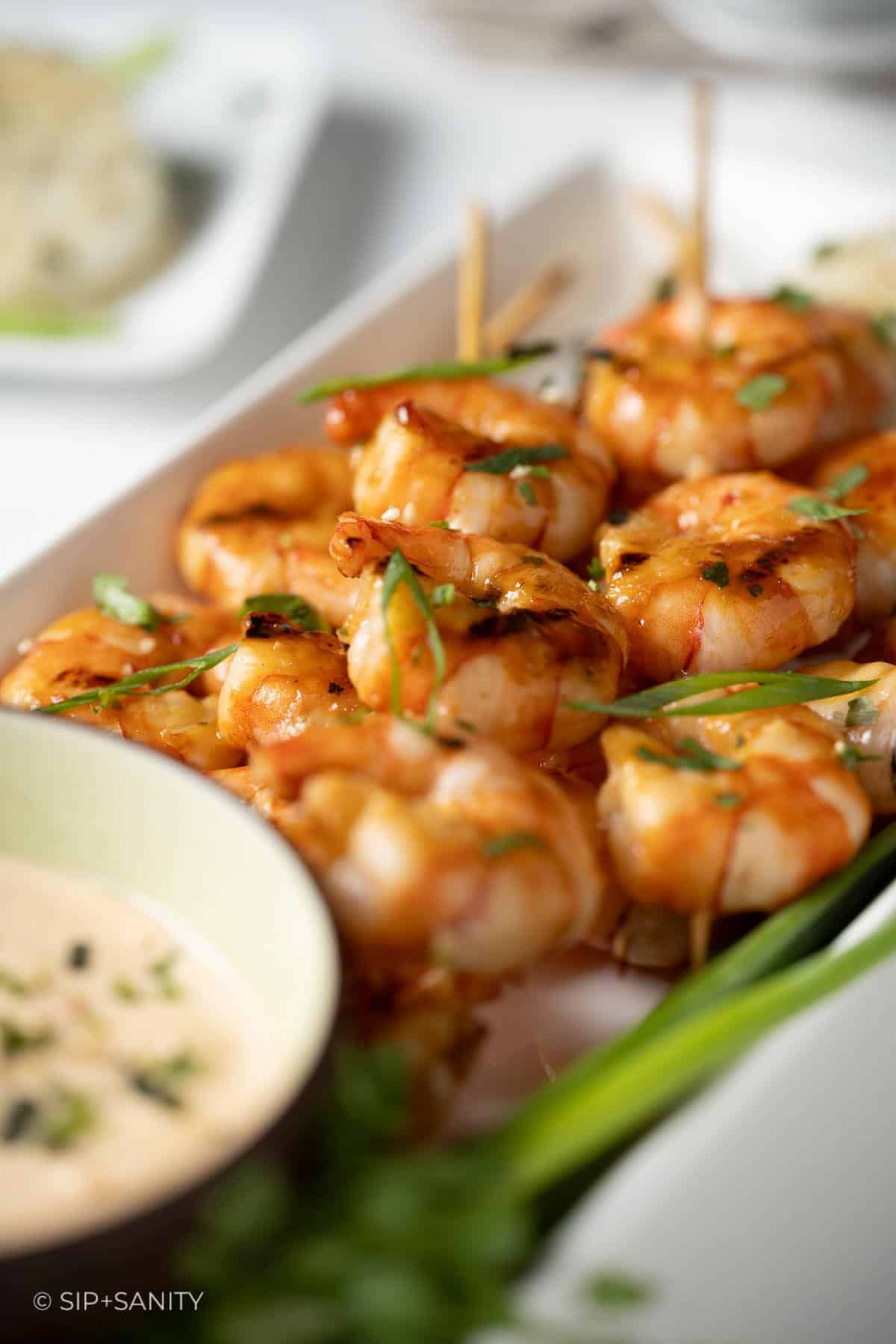Several shrimp skewers arranged on a plate with sliced scallions.