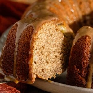 A close-up of a sliced bundt cake with a light brown interior and a shiny caramel glaze drizzling down the sides.