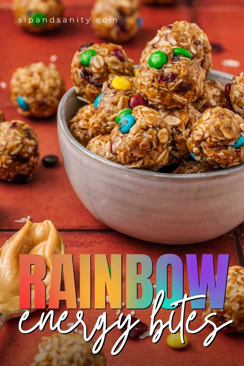 A bowl of oat-based energy bites mixed with colorful mix-ins sits on a red surface; text reads Rainbow Energy Bites.