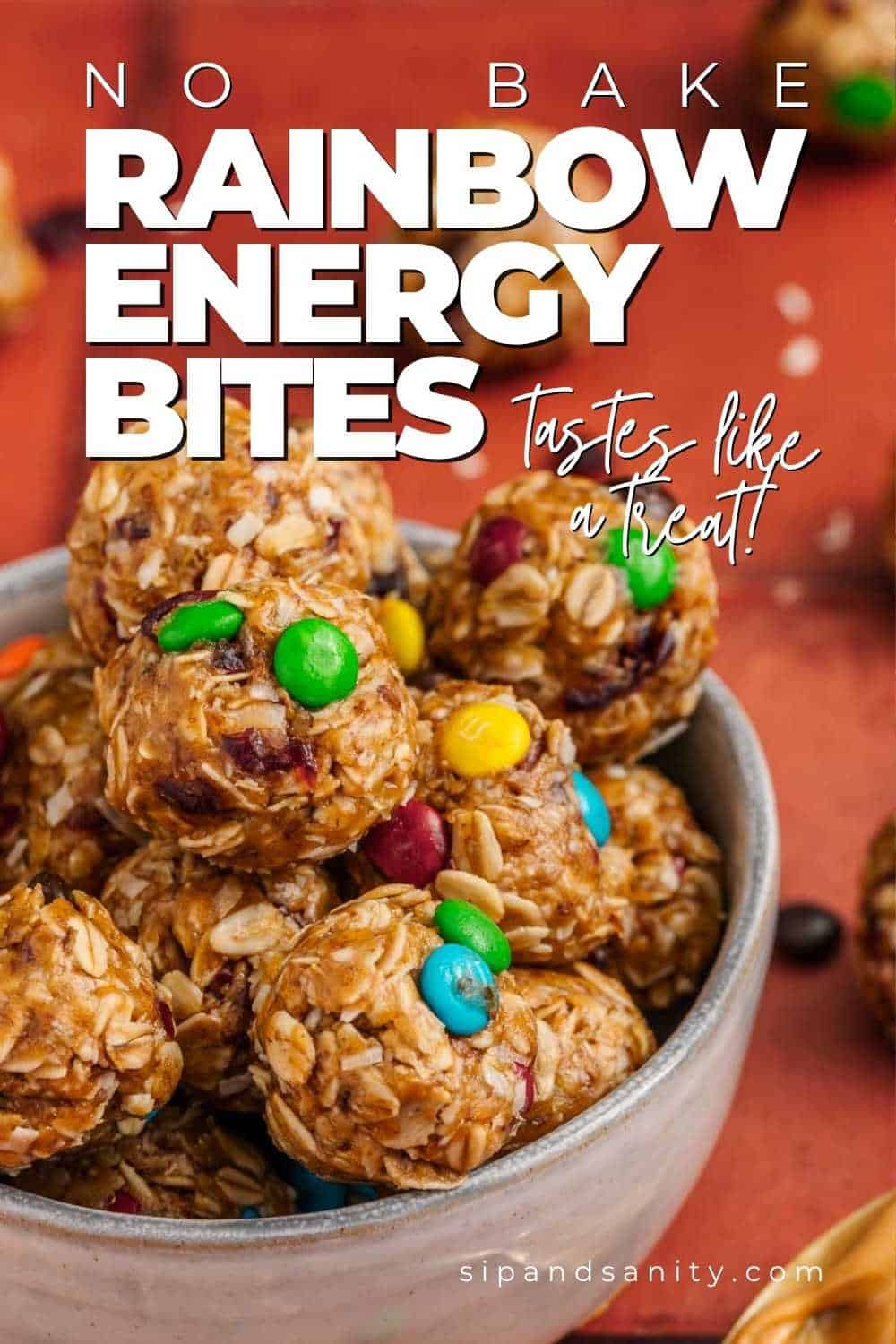 A bowl filled with no-bake energy bites made of oats and colorful candy-coated chocolates, with text overlay reading No Bake Rainbow Energy Bites - Tastes like a treat!.