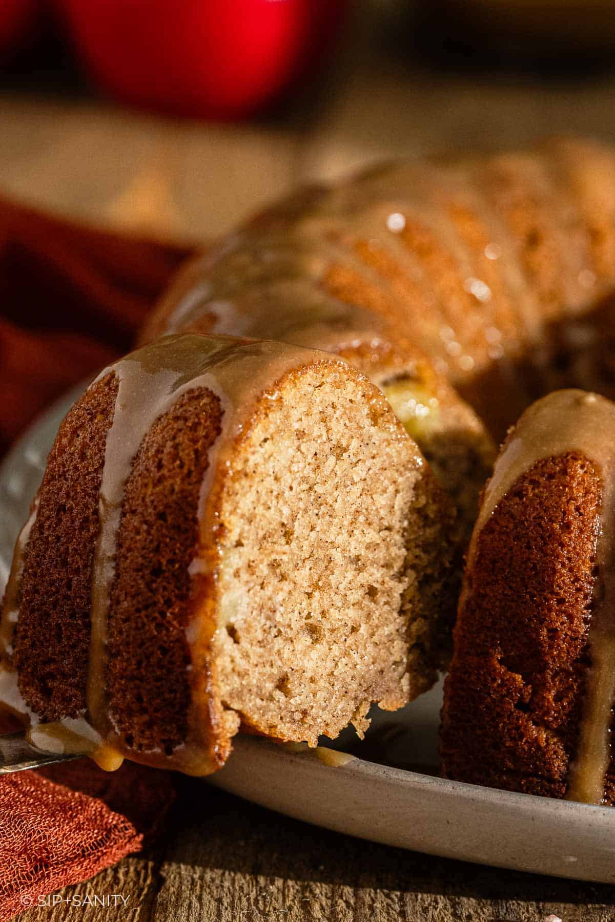 A close-up of a sliced bundt cake with a light brown, moist interior and a shiny glaze drizzled over the top, sitting on a white plate.