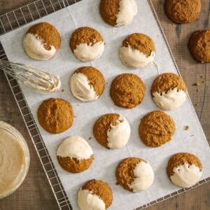 A cooling rack holds parchment paper with pumpkin cookies, some dipped in a light glaze.