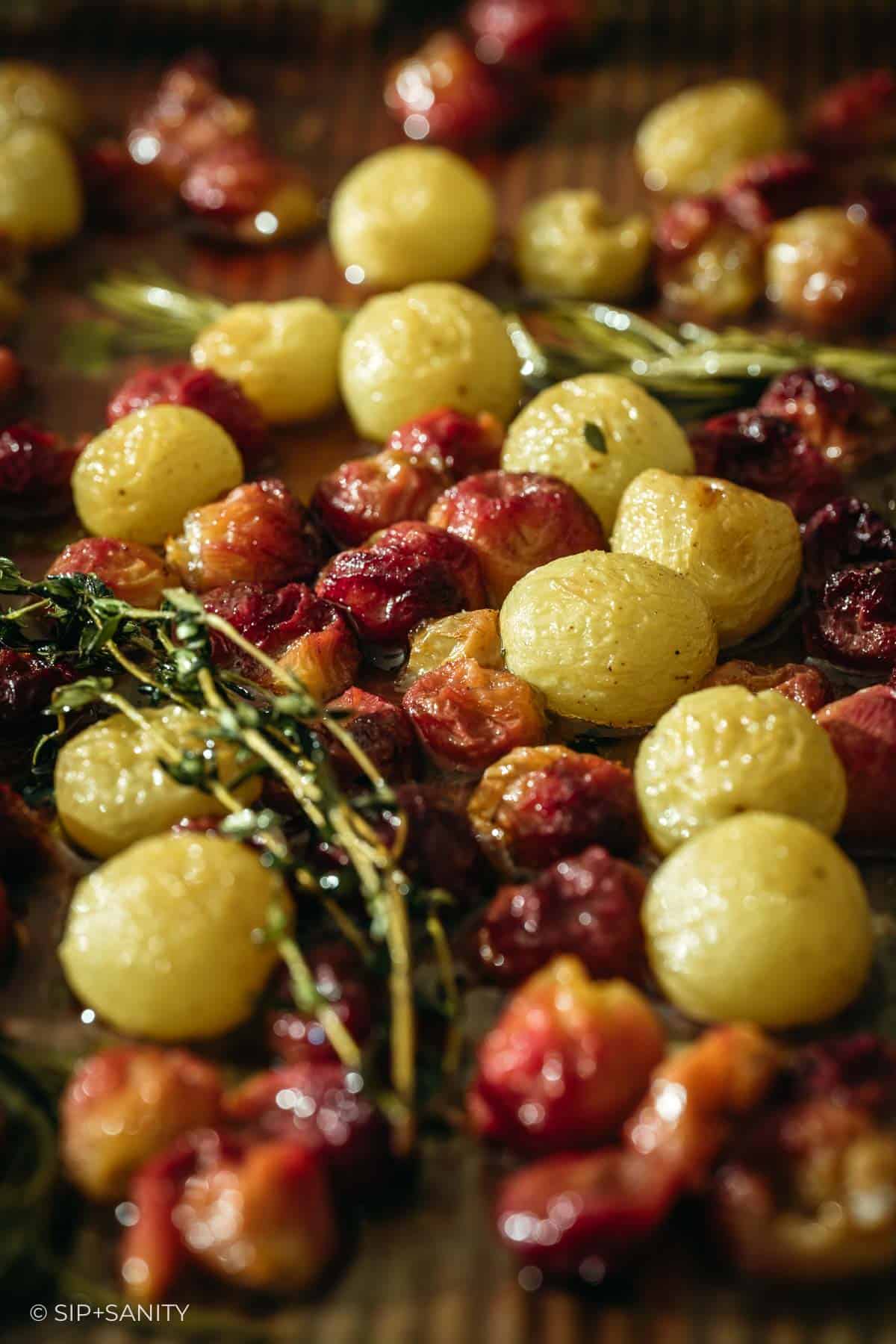 Close-up of roasted green and red grapes with sprigs of fresh herbs on a baking sheet after roasting.