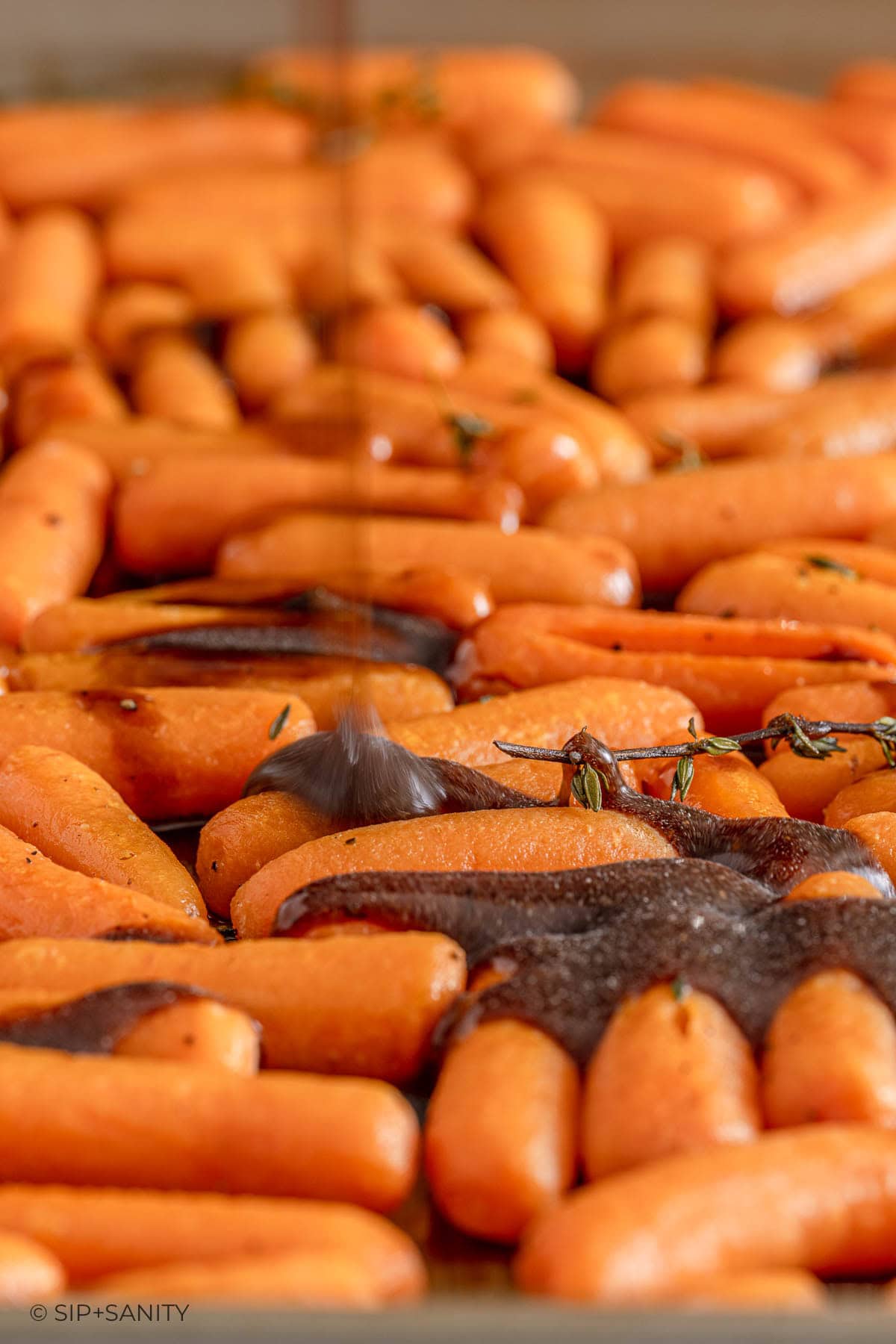 Baby carrots on a baking sheet are drizzled with dark balsamic glaze and topped with sprigs of fresh thyme.