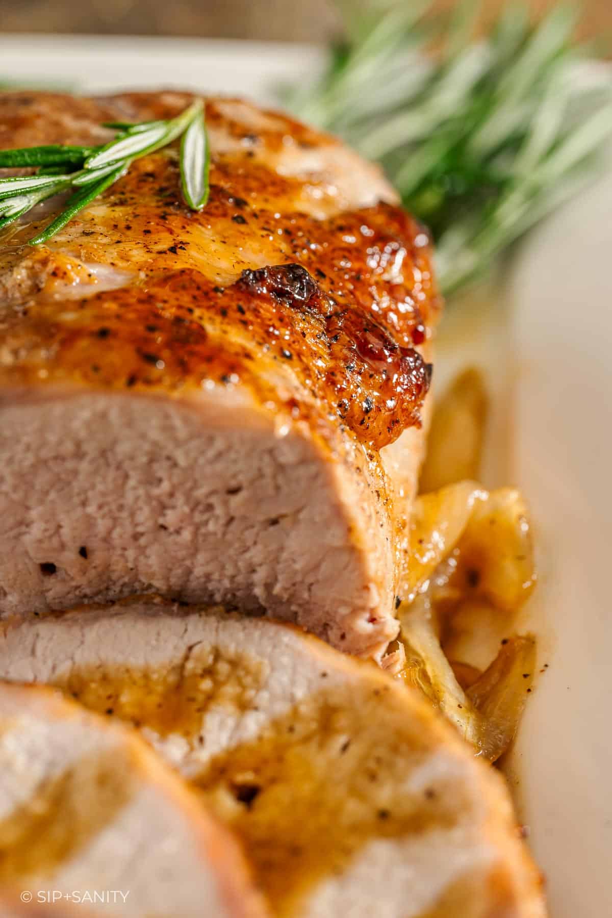 Close-up of a juicy, golden-brown roasted pork loin garnished with fresh rosemary.