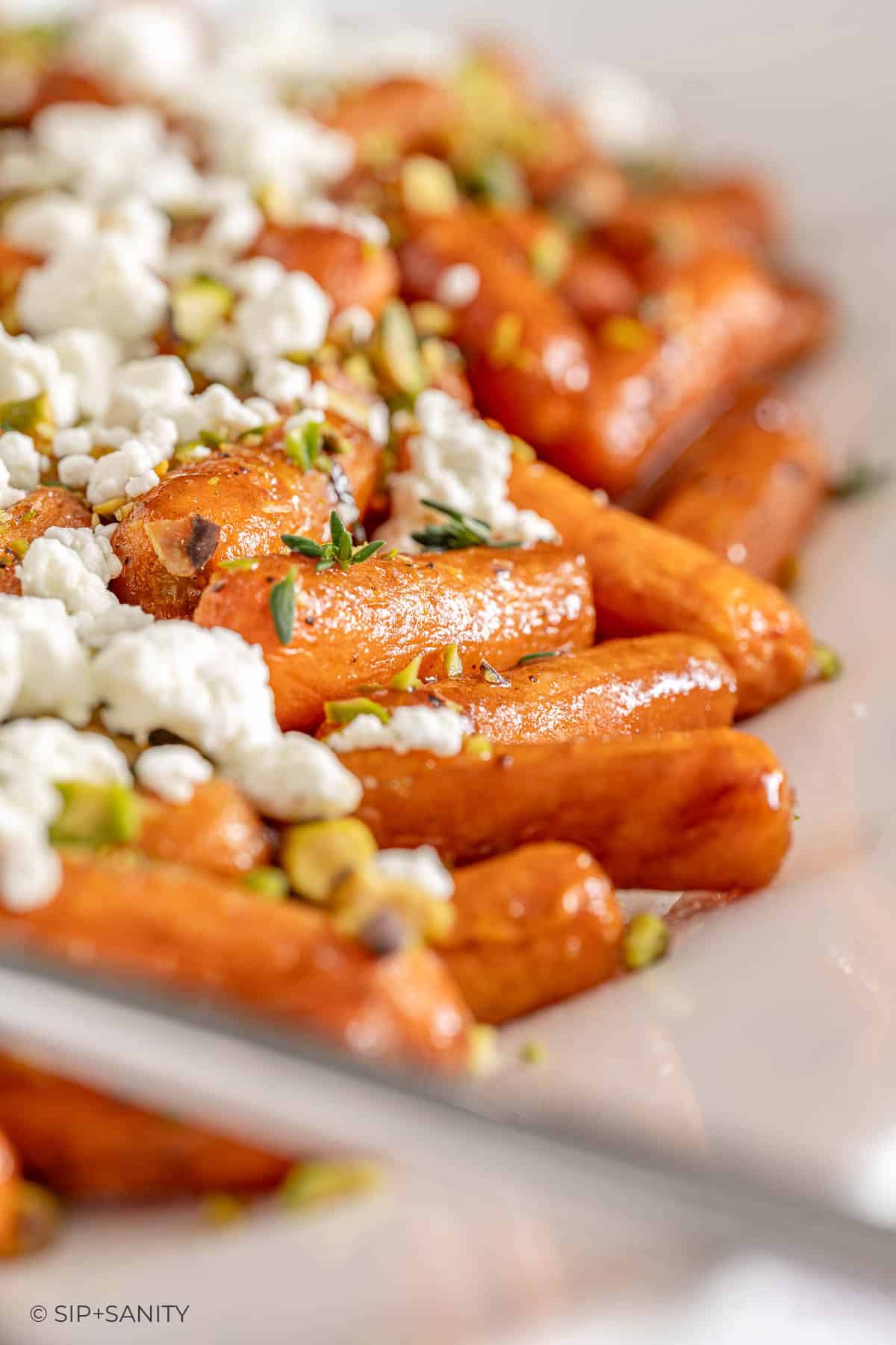 Roasted baby carrots with goat cheese, pistachios, and herbs on a white platter.