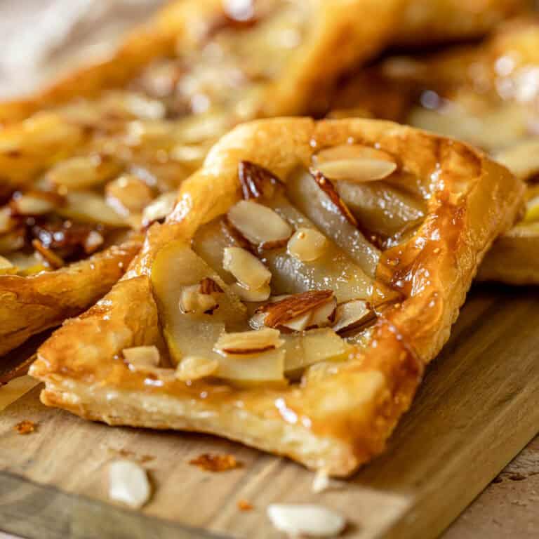 Rectangular pastry with sliced pears and chopped almonds on top, golden flaky crust, glossy finish, on a wooden surface.