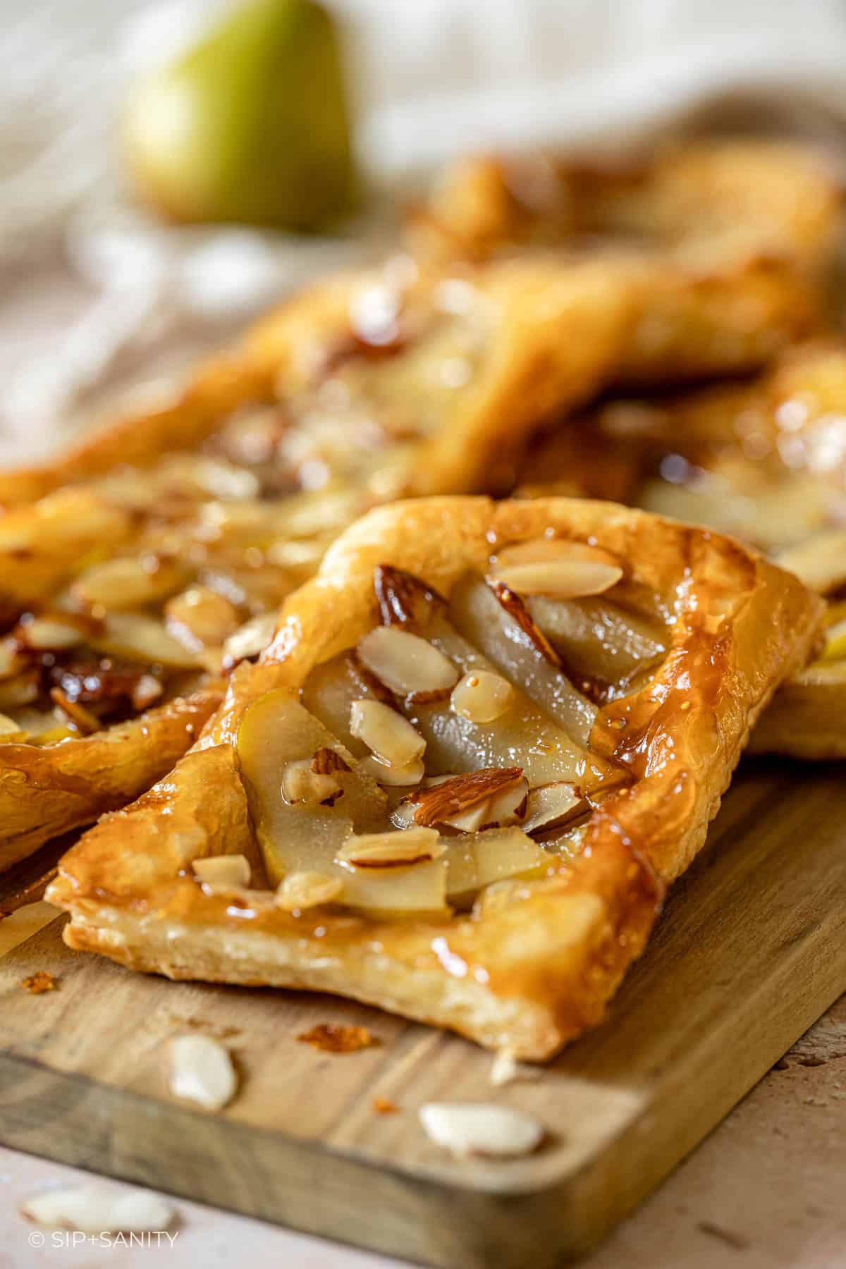 Rectangular puff pastry tarts with pears and almonds on a wooden board, golden, glossy, and freshly baked.
