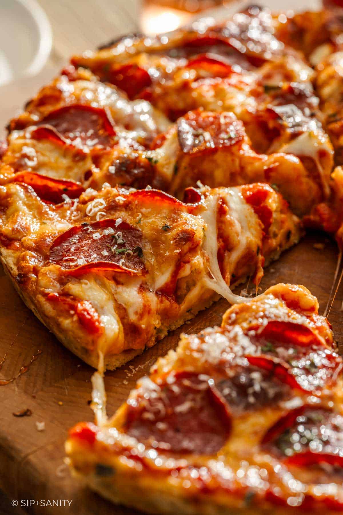 Close-up of hot honey pizza with stretchy melted cheese, tomato sauce, pepperoni slices, and grated cheese on wood.