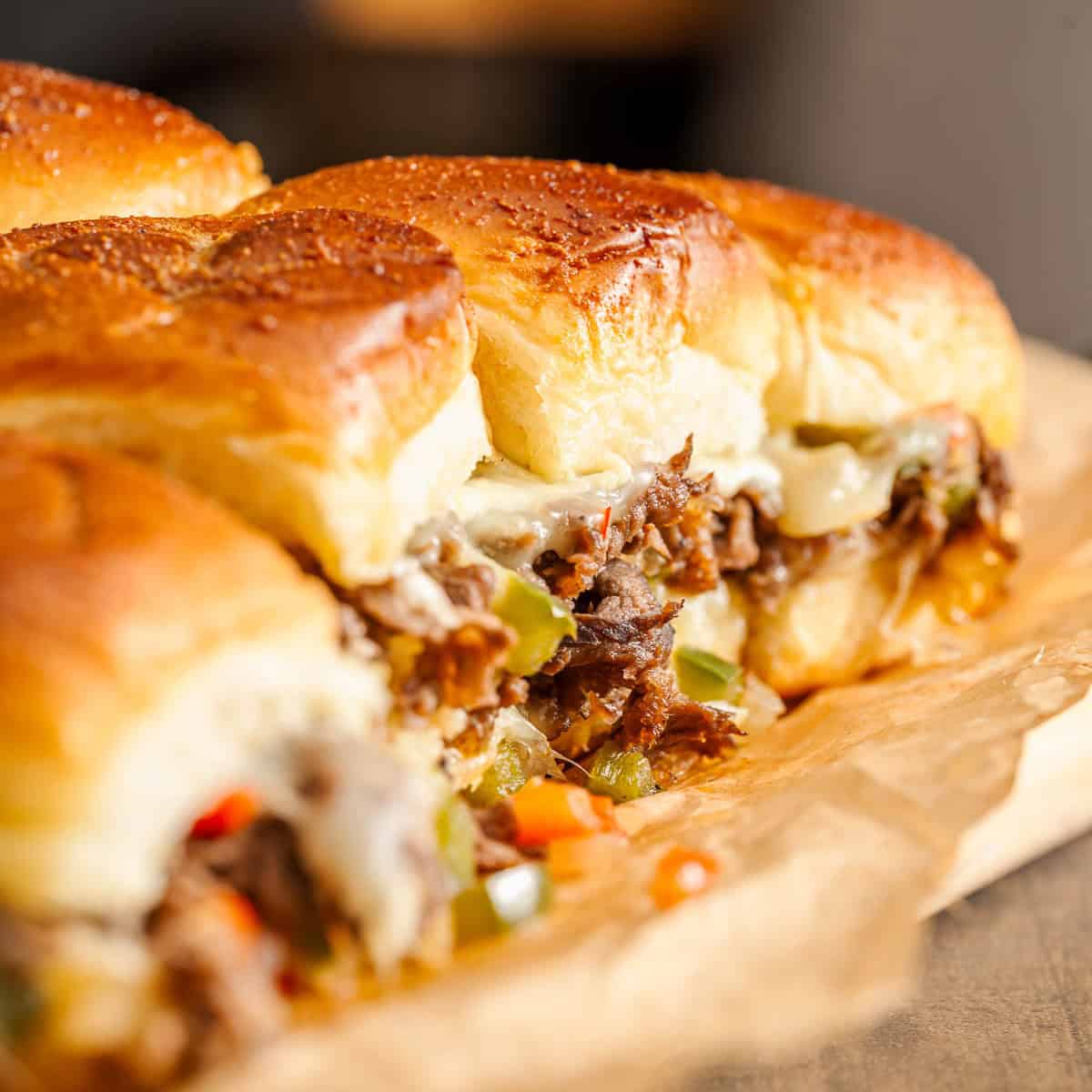 Cheesesteak sliders with shredded beef, melted cheese, and diced bell peppers on parchment paper.