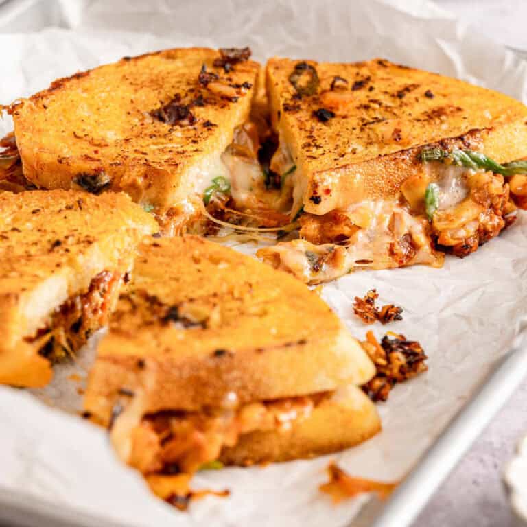 Kimchi grilled cheese sandwich quartered, with melted cheese and veggies on crispy bread. Filling oozes onto parchment paper.