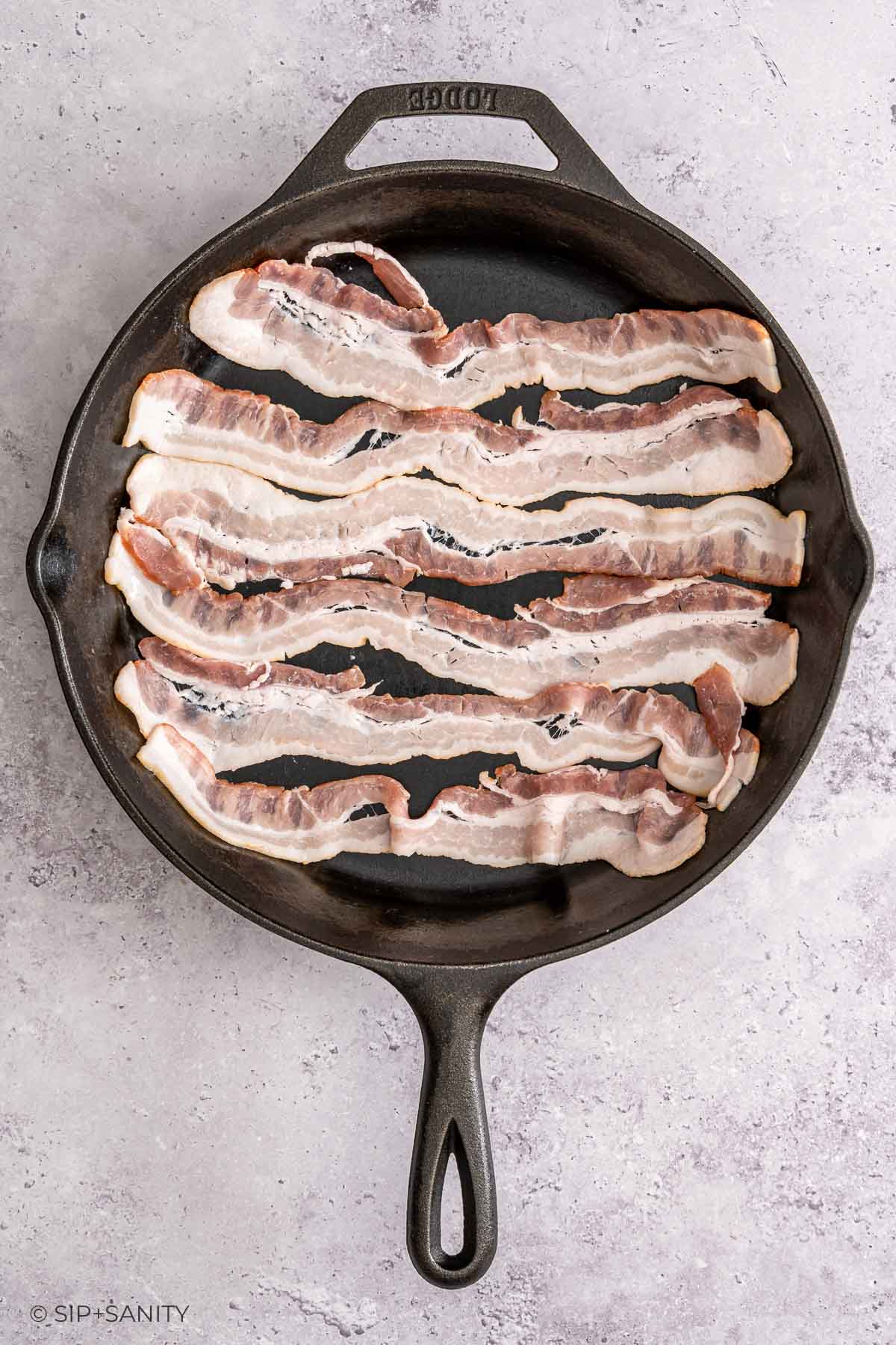 Five raw bacon strips in a black cast iron skillet sit side by side on a light countertop.
