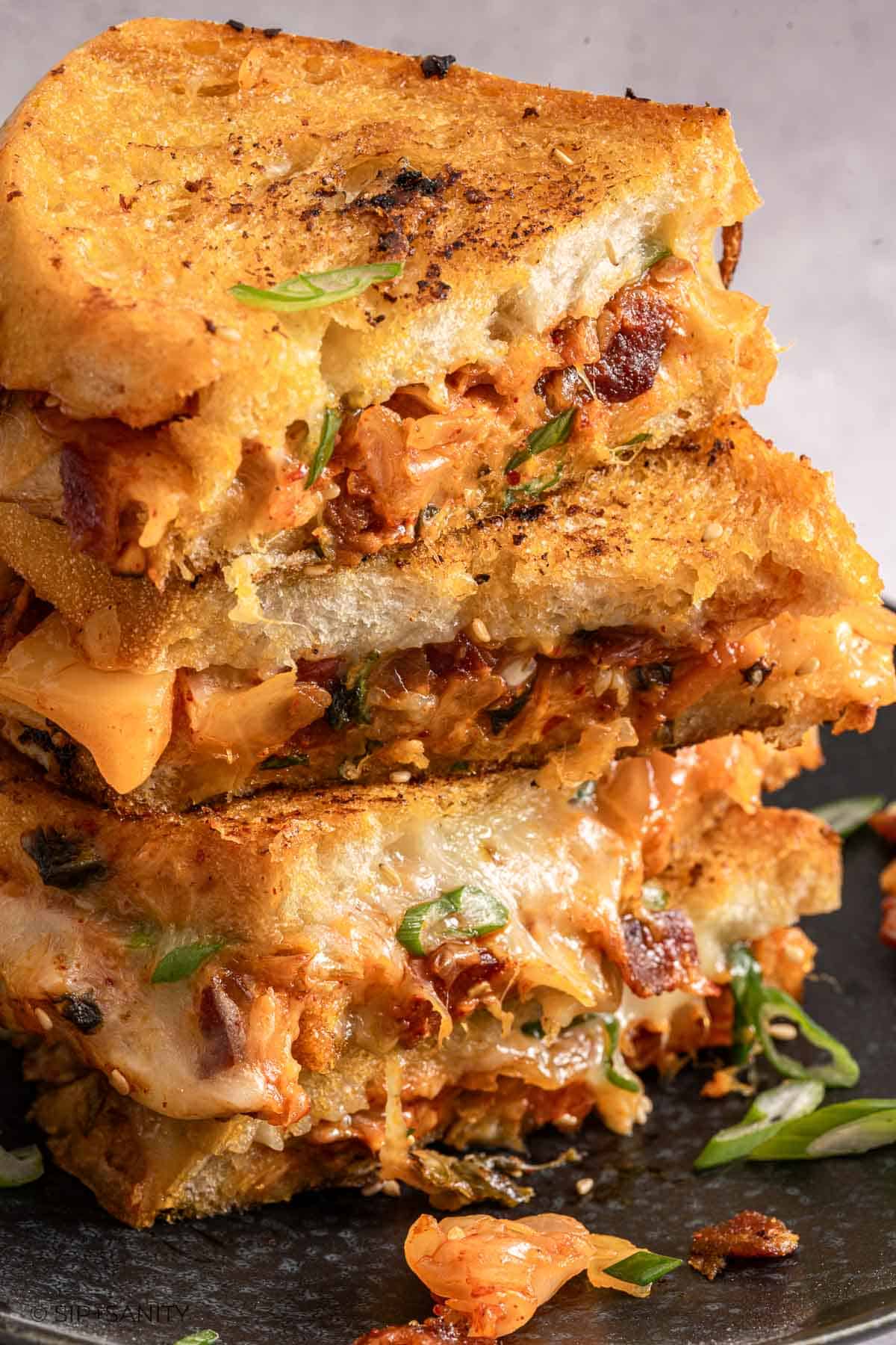 Stacked kimchi grilled cheese halves with melted cheese, crispy bacon, green onions, and golden toasted bread oozing cheese.