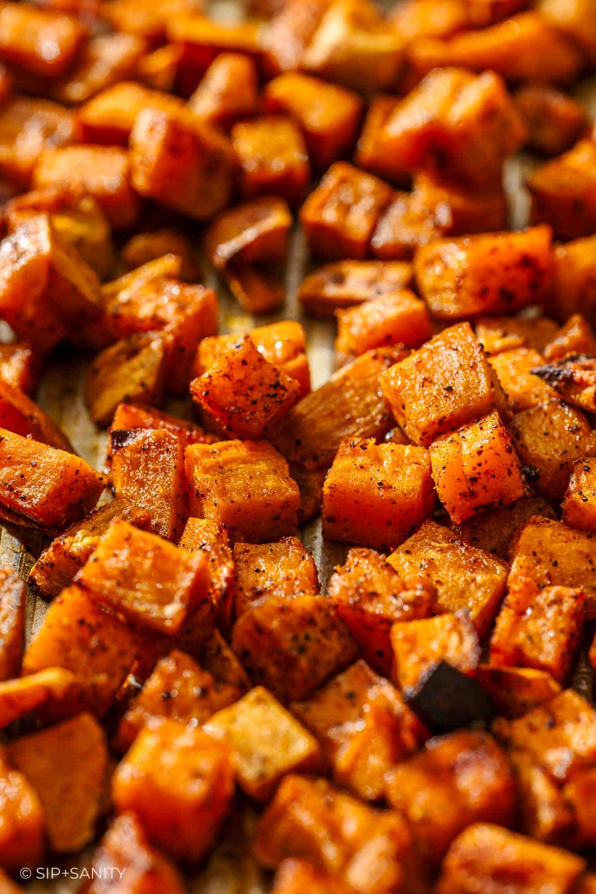 Roasted sweet potato cubes, golden brown and crispy, seasoned with spices on a baking sheet, close-up view.