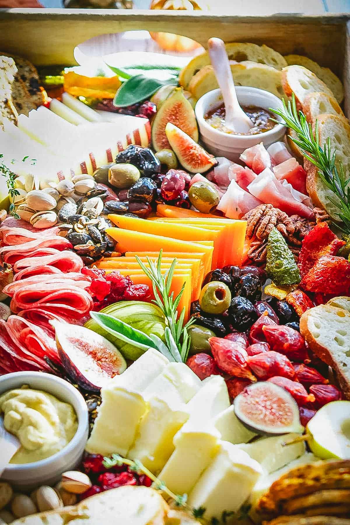 A vibrant charcuterie board with cheese, meats, figs, olives, nuts, bread, fruit & dips. Garnished and neatly arranged.