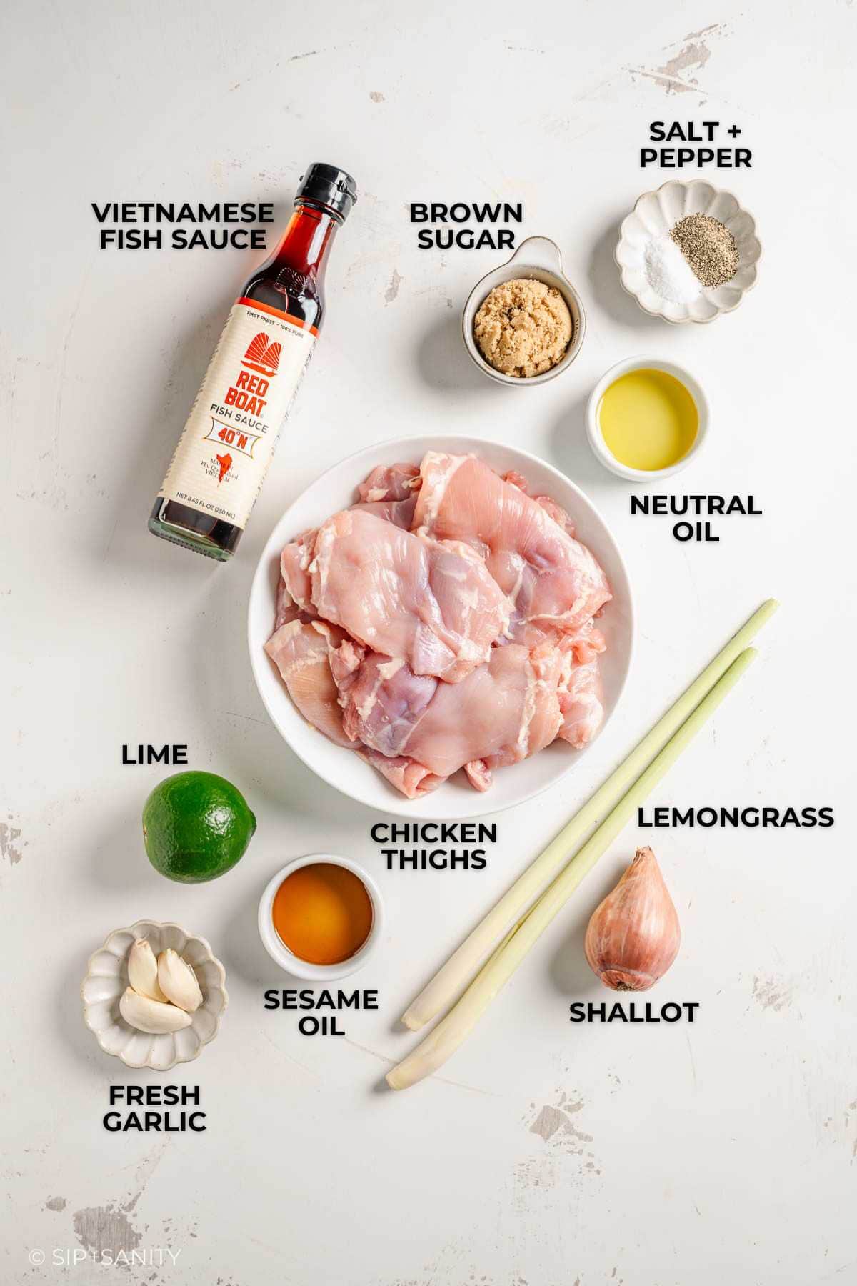 Flat lay of labeled Vietnamese ingredients: chicken thighs, fish sauce, lime, sesame oil, lemongrass, garlic, more.