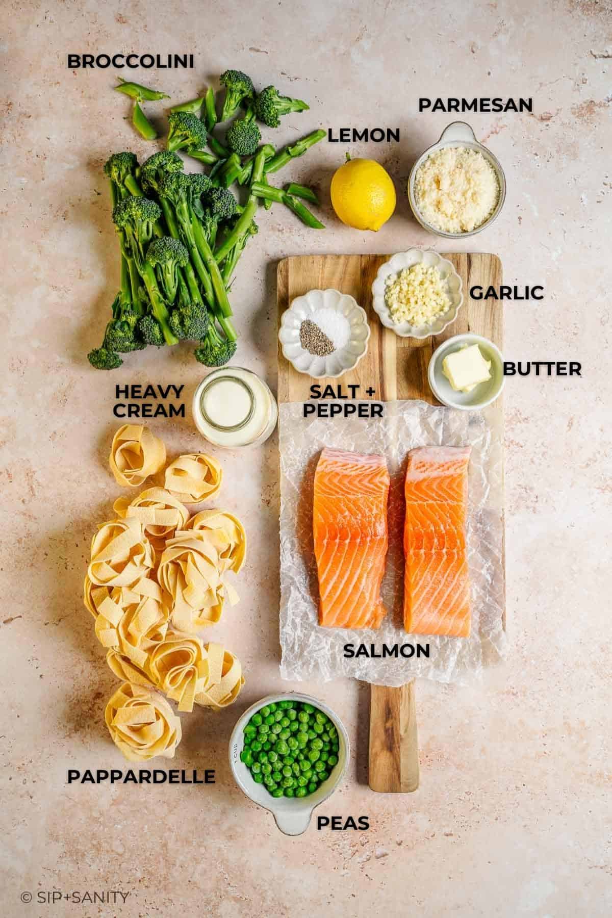 Overhead shot of labeled pasta ingredients: broccolini, lemon, parmesan, salmon, pappardelle, peas, cream, butter, garlic.