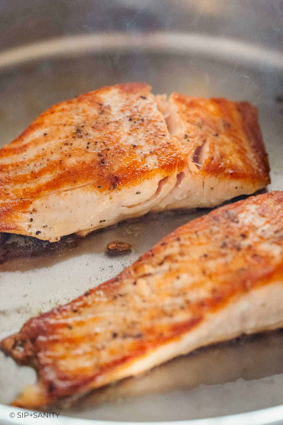 Pan-seared salmon fillets with golden-brown crust cooking in a stainless steel skillet.