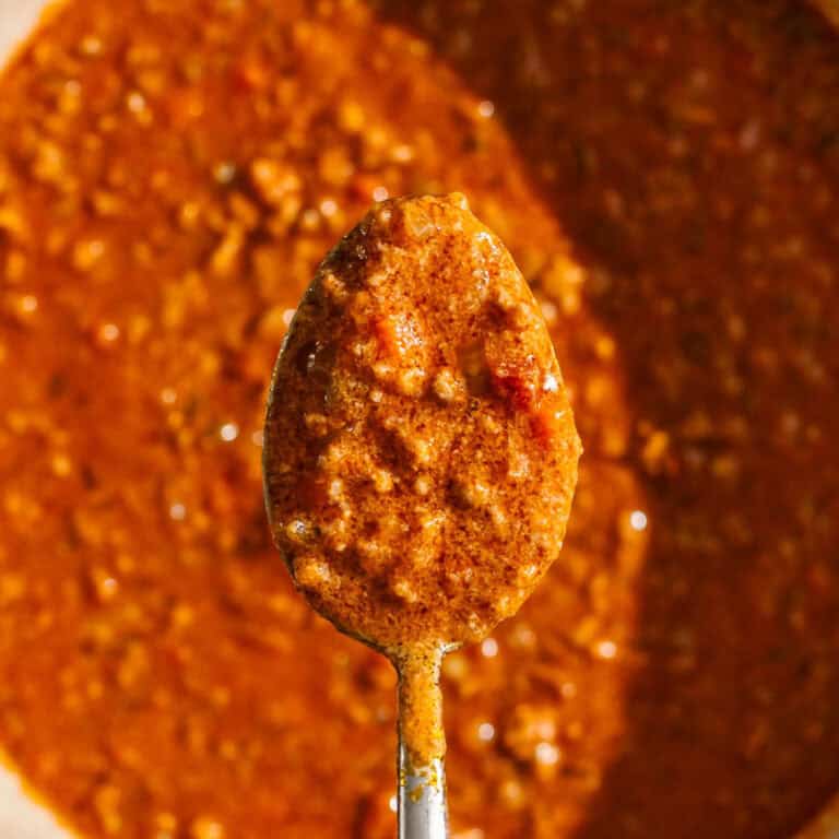 A spoonful of bolognese with bechamel sauce held above a pot of the sauce.