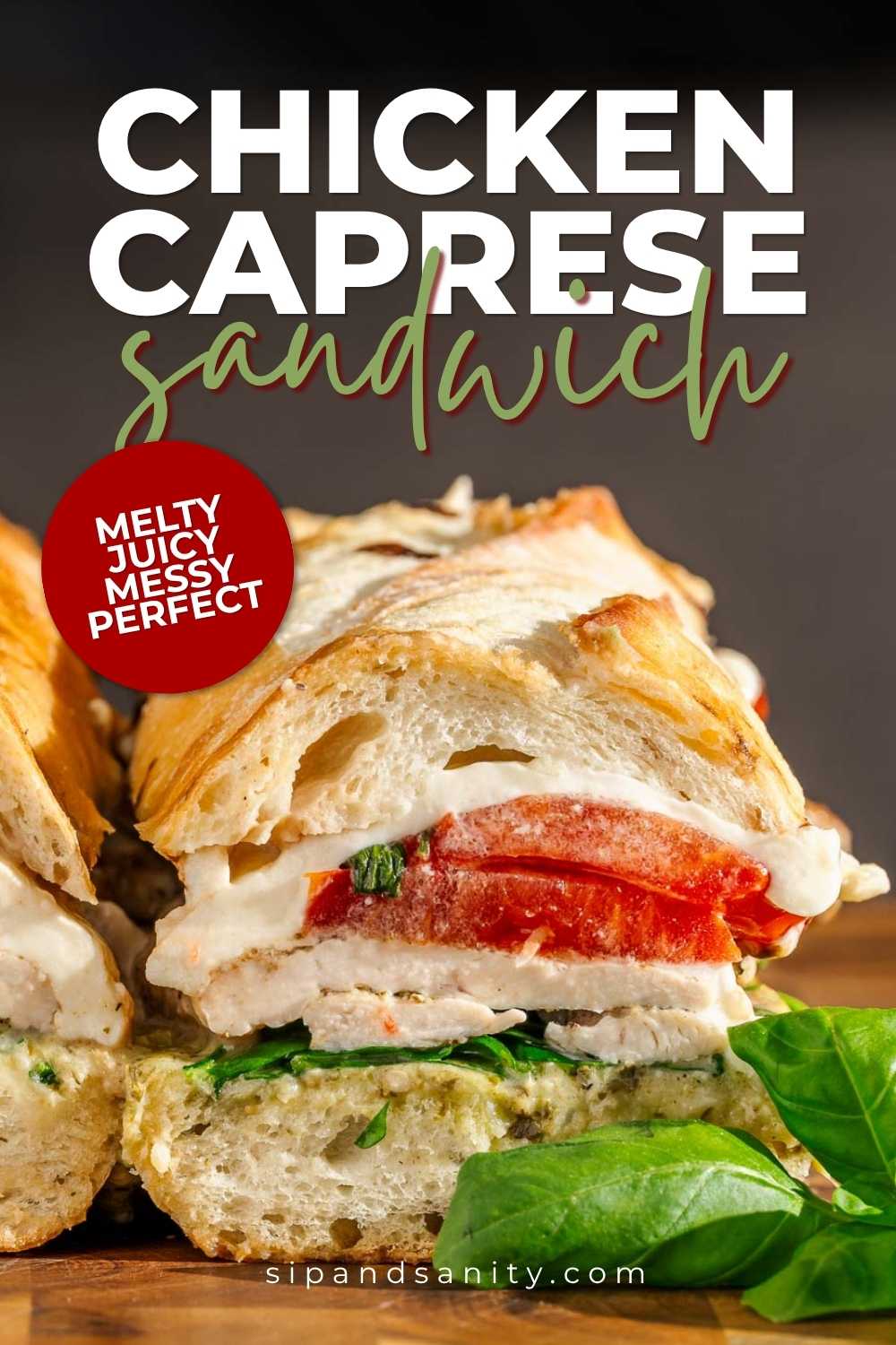 Chicken caprese sandwich with melted cheese, tomato, basil, and chicken on crusty bread. Basil leaves in foreground.