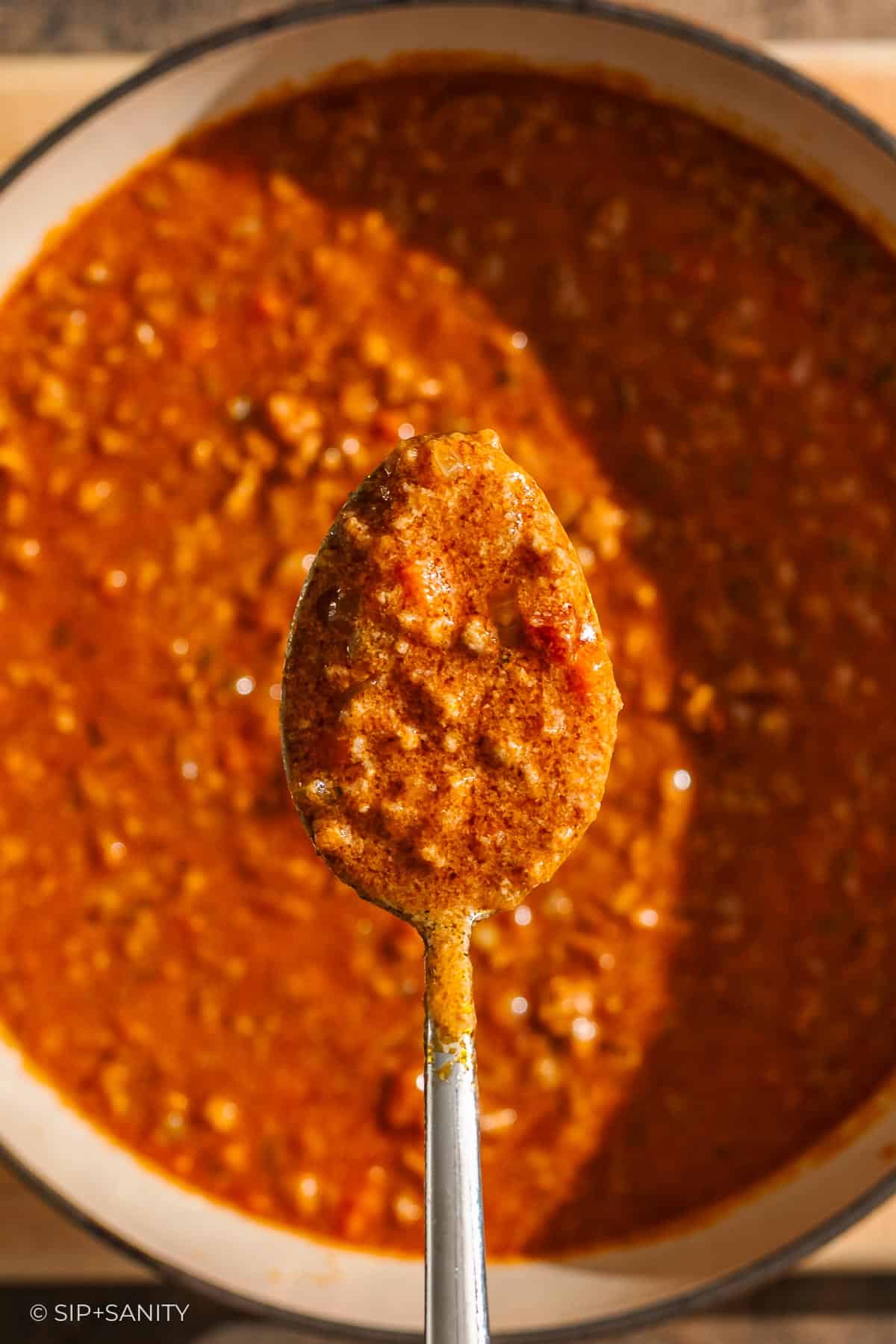 A spoonful of thick, chunky bolognese with bechamel sauce held above a pot containing more of the same meat sauce.