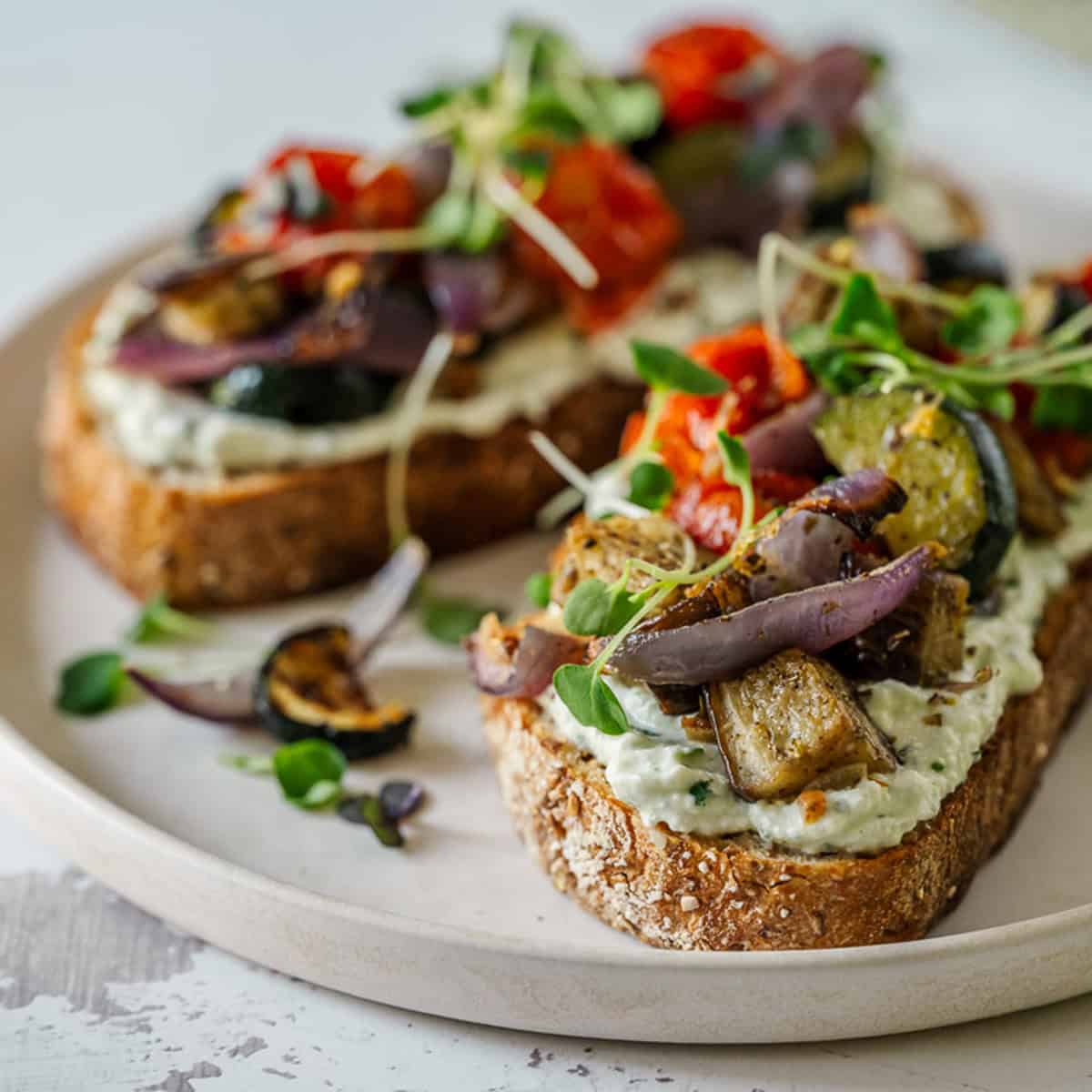 Whole grain bread slices with cottage cheese spread, grilled veggies, cherry tomatoes, and greens on a light plate.