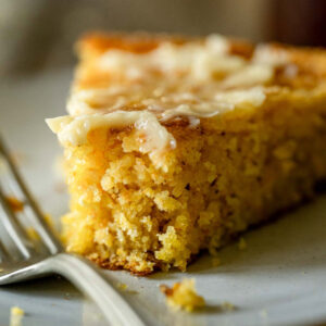 Slice of cornbread with melted salted honey butter on a white plate, fork next to it.