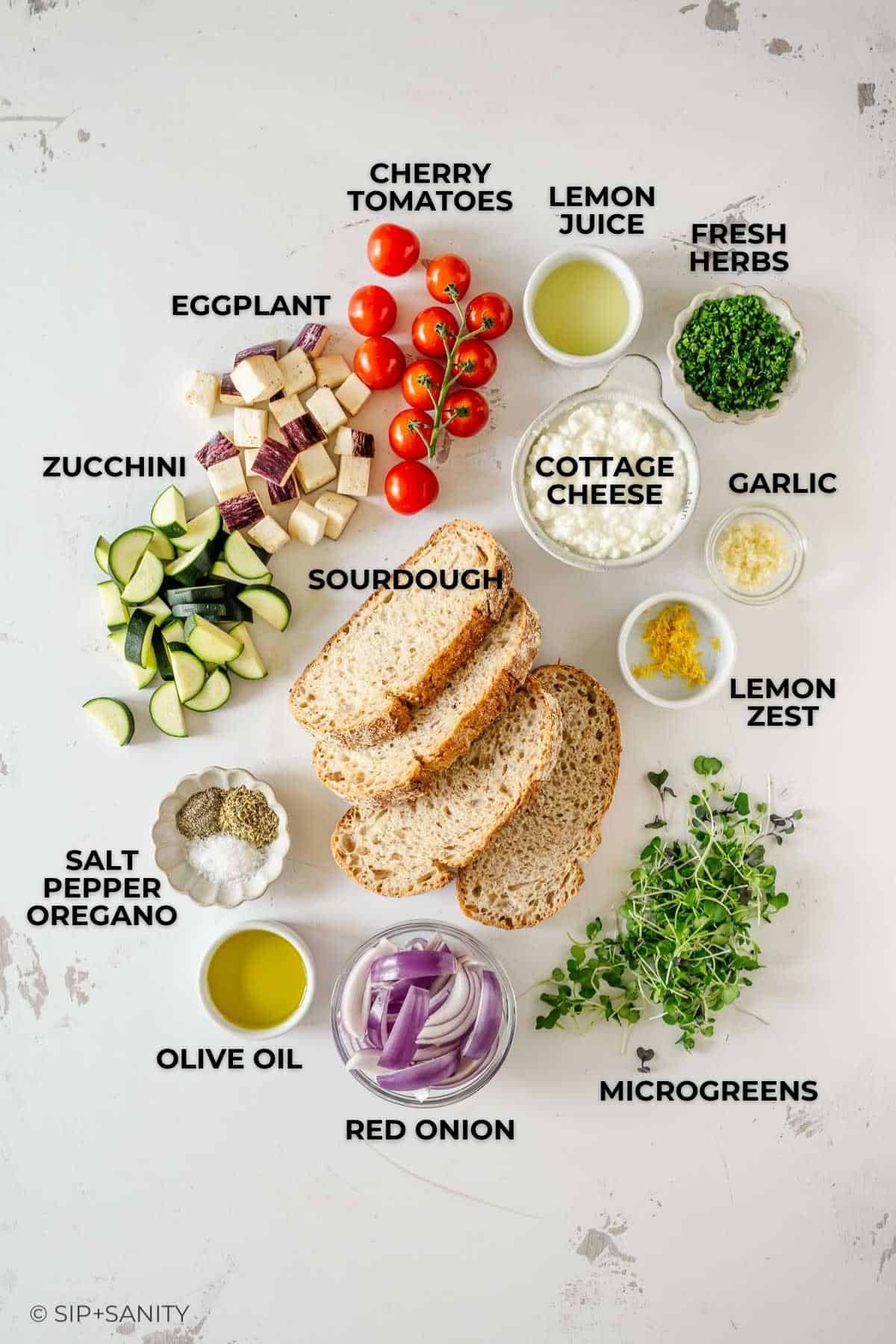Flat lay of labeled ingredients: cherry tomatoes, lemon, herbs, cottage cheese, garlic, onion, olive oil, veggies, bread.