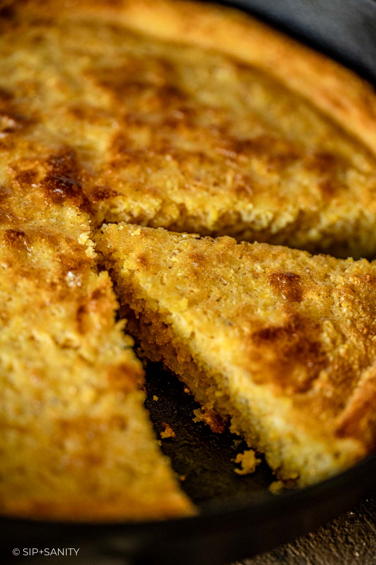 Golden brown cornbread in a skillet with a wedge missing, revealing its moist and crumbly inside.