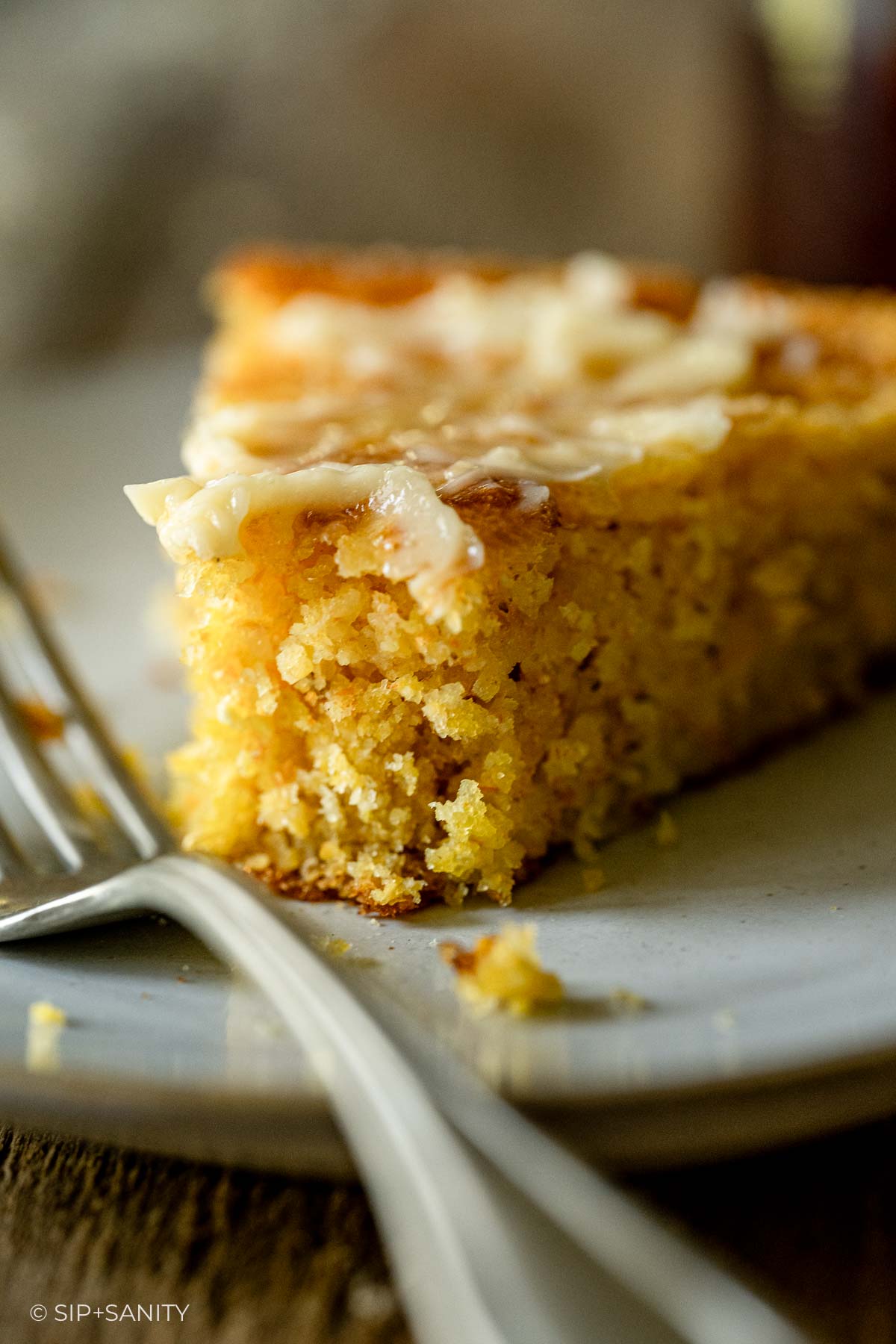 Close-up of golden, crumbly cornbread with melting butter on a plate, fork beside it. The cornbread looks moist.