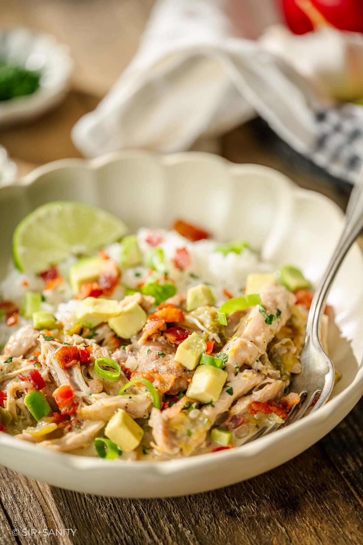 Shredded chicken, avocado, red peppers, and green onions over rice with lime garnish; fork in bowl.