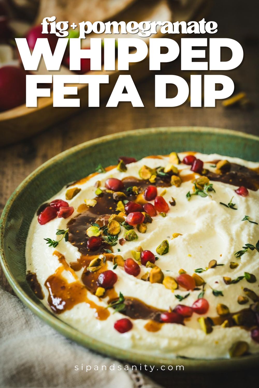 A bowl of whipped feta dip topped with fig, pomegranate, pistachios, and herbs. Text: fig + pomegranate whipped feta dip.