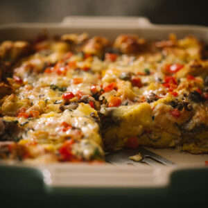 Baked breakfast casserole with sausage, peppers, and melted cheese in a baking dish with a spatula.