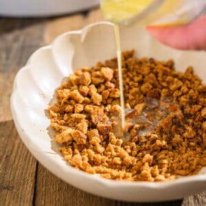 Melted butter being poured over a bowl of crushed gingersnap cookie crumbs.