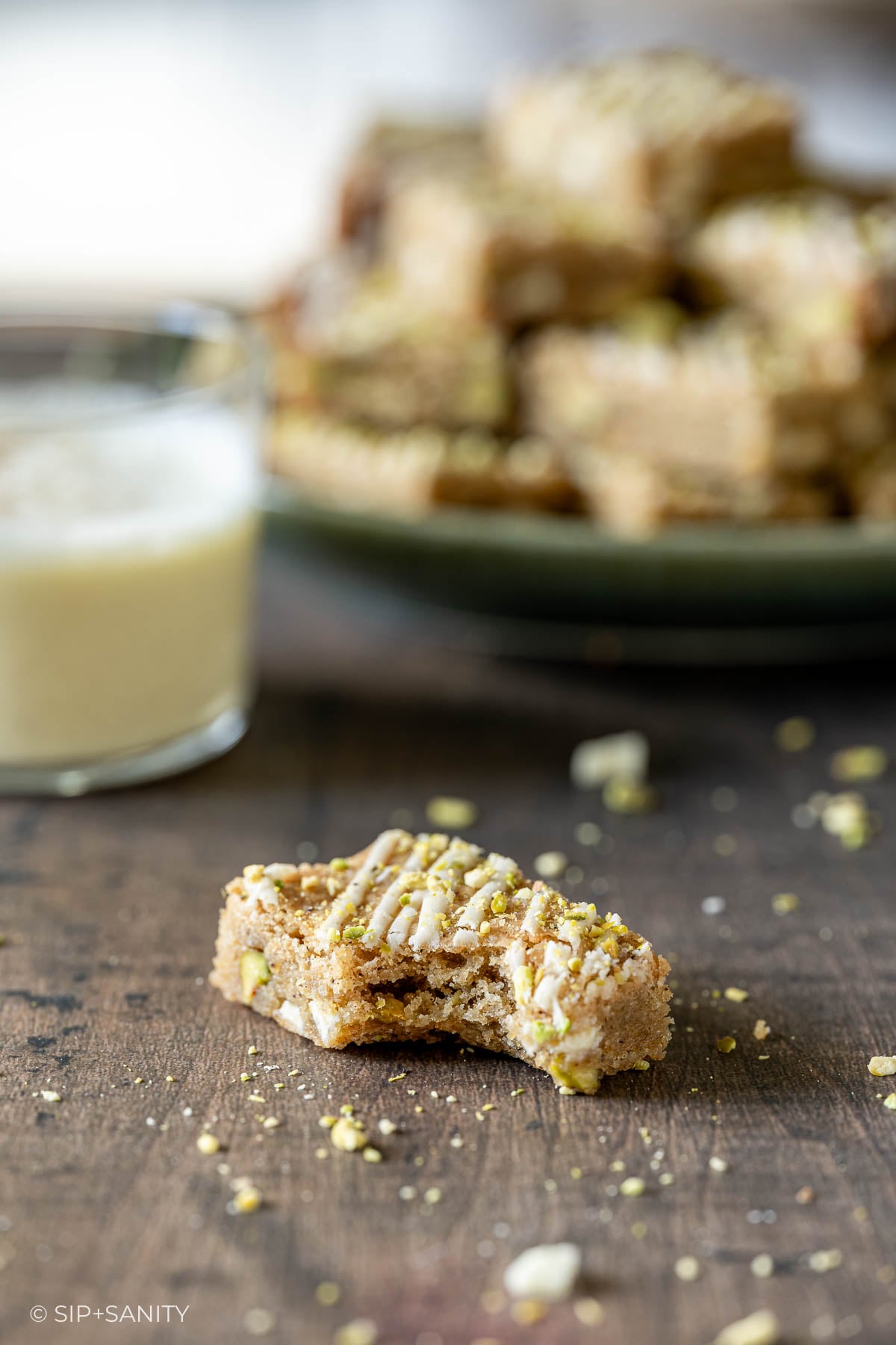 A bitten eggnog blondie bar with white icing, with more bars and a glass of milk in the background.