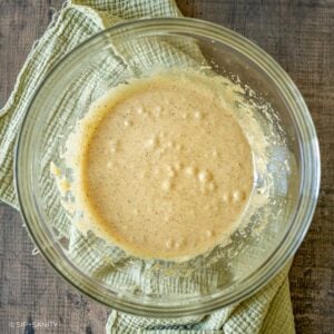 A glass mixing bowl filled with light brown, speckled liquid batter.