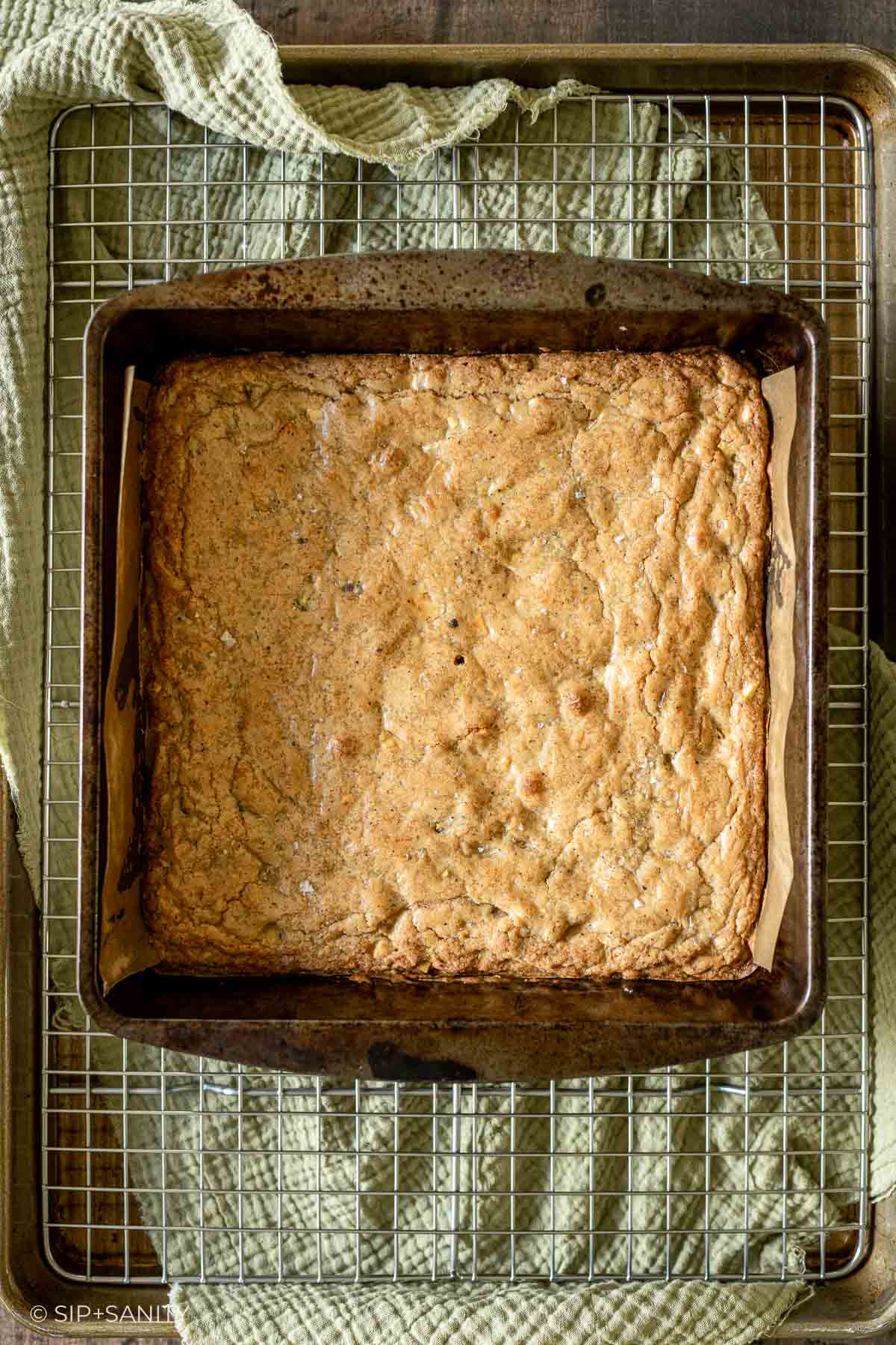 Square pan of baked eggnog blonde brownies in a metal dish on a wire cooling rack.
