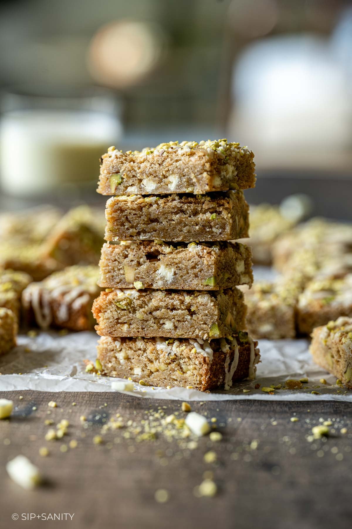 Five square eggnog blondie bars stacked, topped with chopped pistachios and white chocolate drizzles.