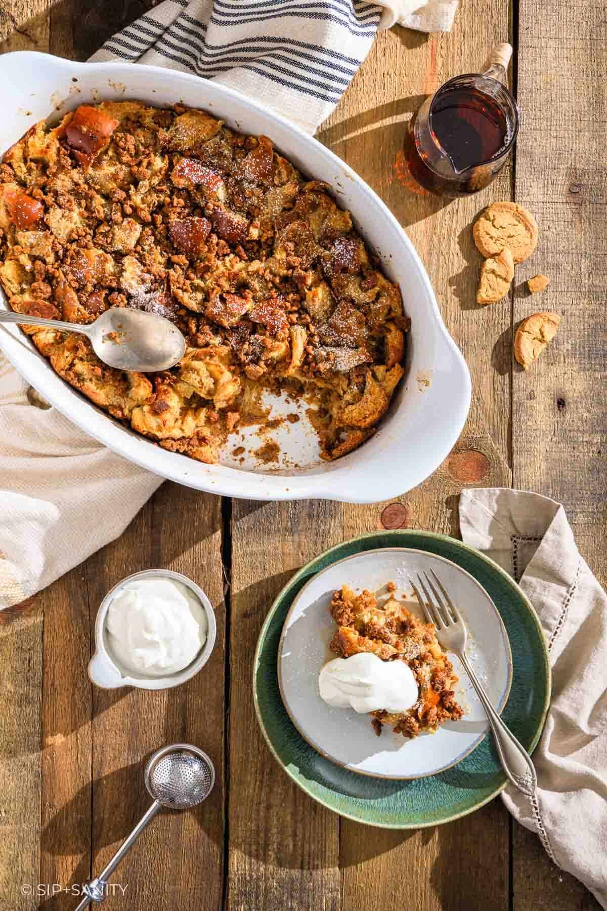 Gingerbread eggnog french toast casserole with cream on a plate, set next to a full baking dish.