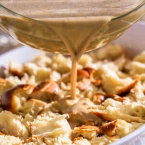 Custard being poured over cubed bread in a baking dish.