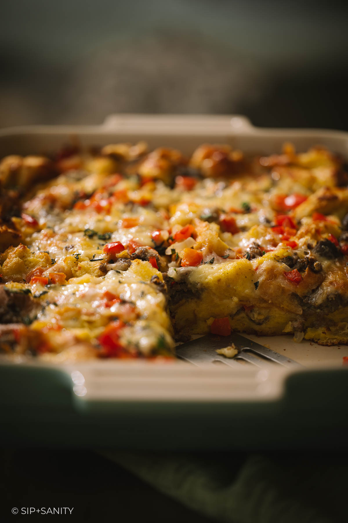 Baked breakfast casserole with sausage, red peppers, and melted cheese in a square dish.