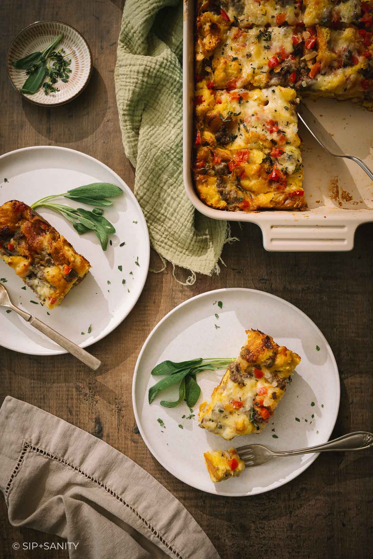 Slices of sausage and vegetable breakfast casserole served on plates with fresh sage, beside a baking dish.